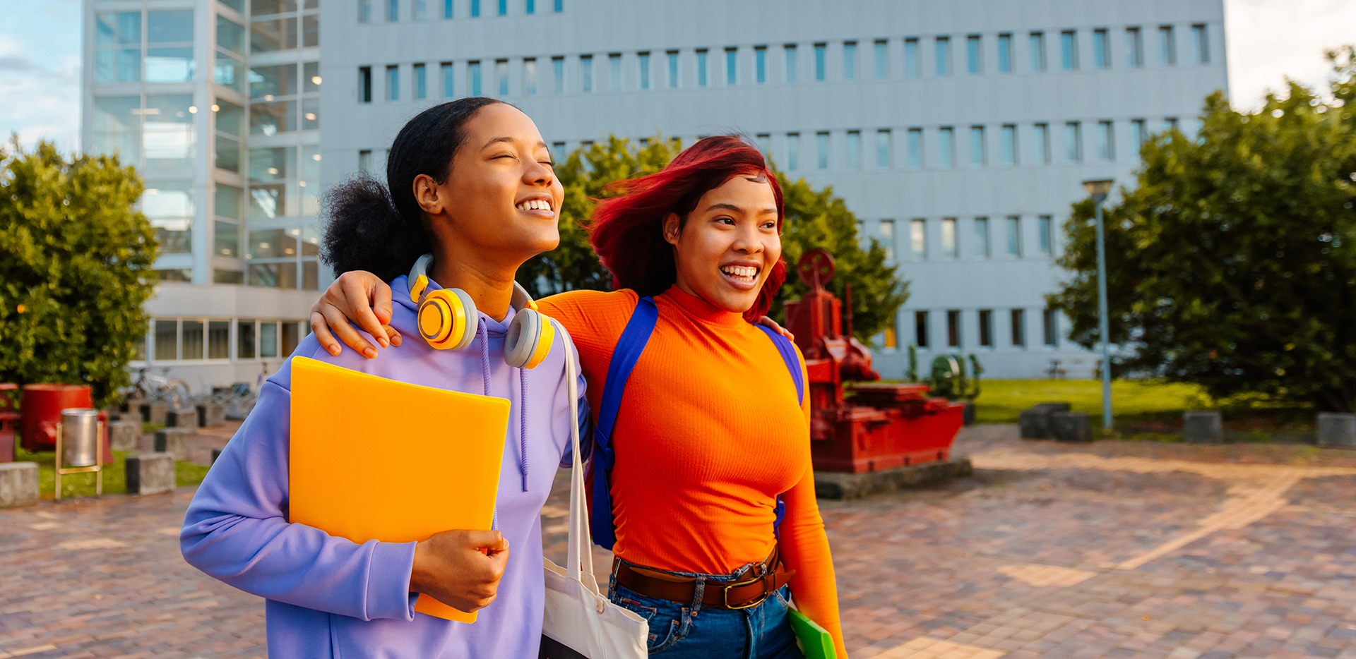 Two students walking towards the sunset, smiling with their arms on each other's shoulders